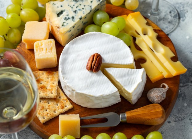Tasting cheese dish on a wooden plate. Food for wine and romantic date, cheese delicatessen on a light concrete background