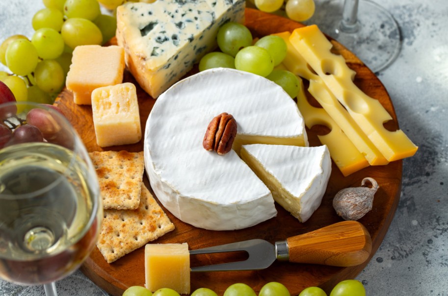 Tasting cheese dish on a wooden plate. Food for wine and romantic date, cheese delicatessen on a light concrete background