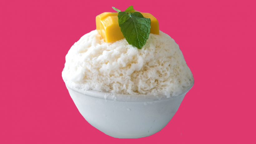 Snow cream in a white bowl topped with mango chuinks and a mint leaf. 