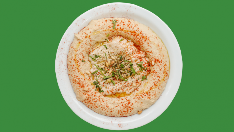 Hummus served in a white bowl and garnished with chopped herbs.