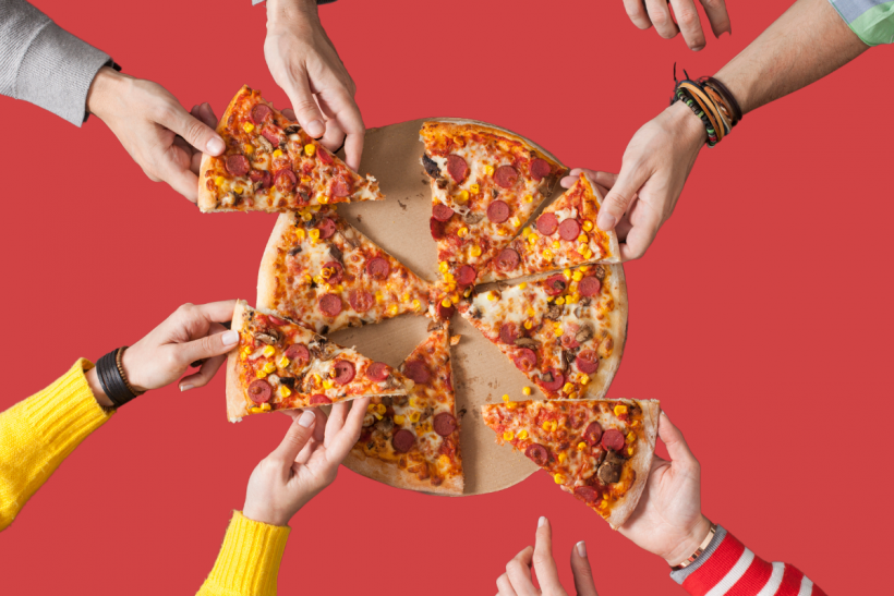 Hands grabbing slices of pizza from a pizza pie.